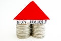 Ã¢â¬ÅBuy houseÃ¢â¬Â text on two piles of coins with red wooden piece forming a small house